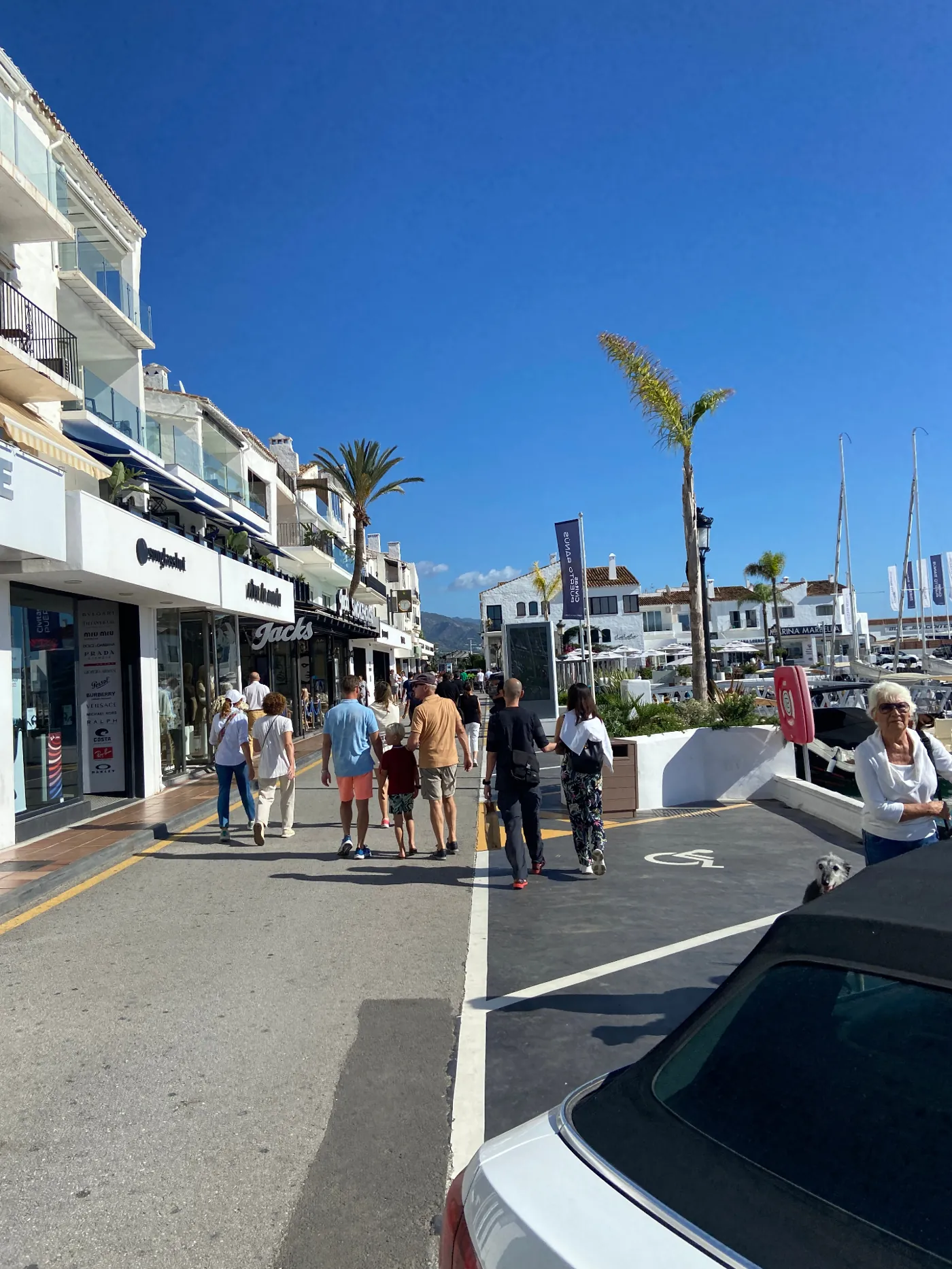 People strolling the waterfront promenade beside the shops and yachts of Puerto Banús
