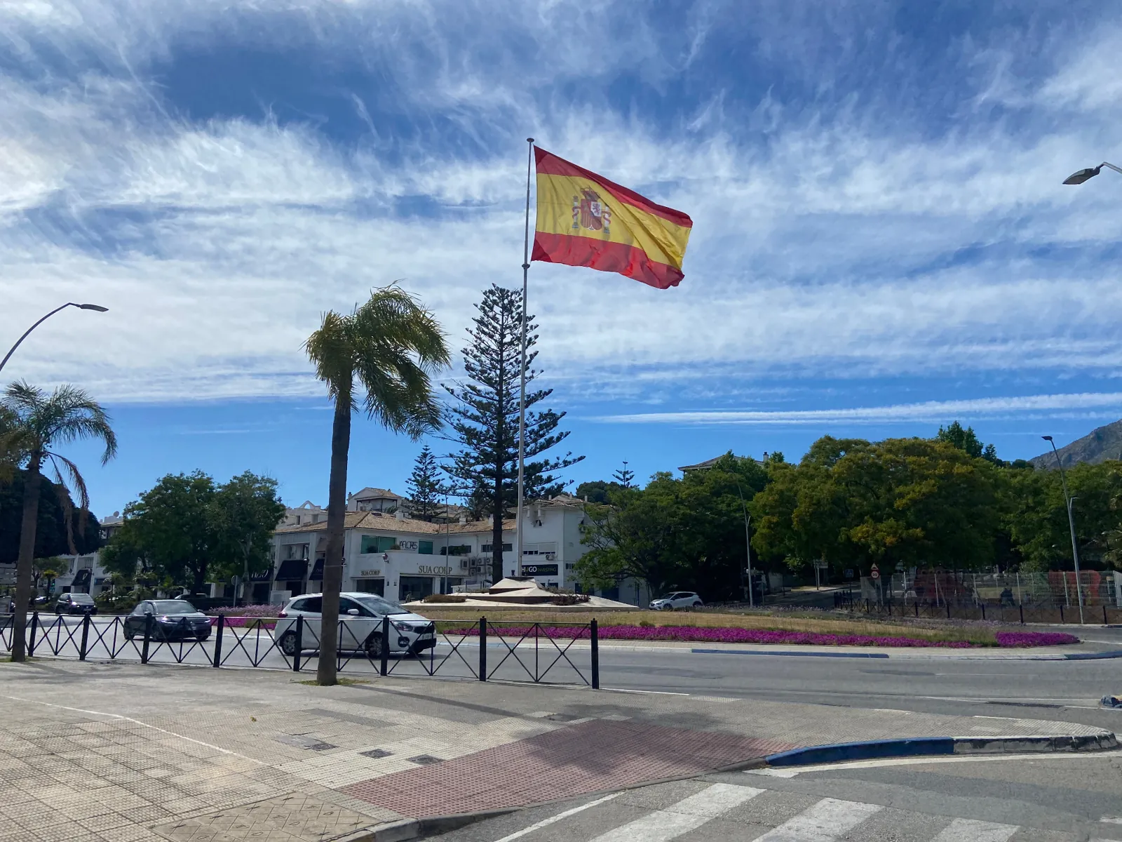 Spanish flag flying over a landscaped roundabout on Marbella's Golden Mile with the Sierra Blanca mountains behind
